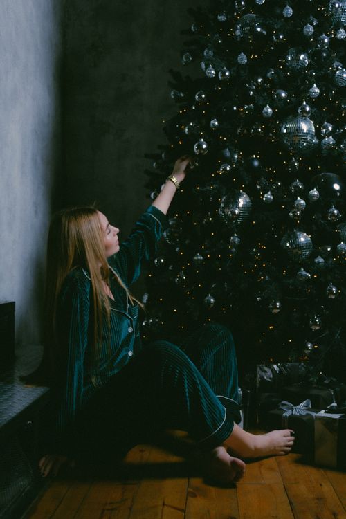 Free A woman in pajamas sits barefoot next to a Christmas tree, creating a cozy winter ambiance. Stock Photo