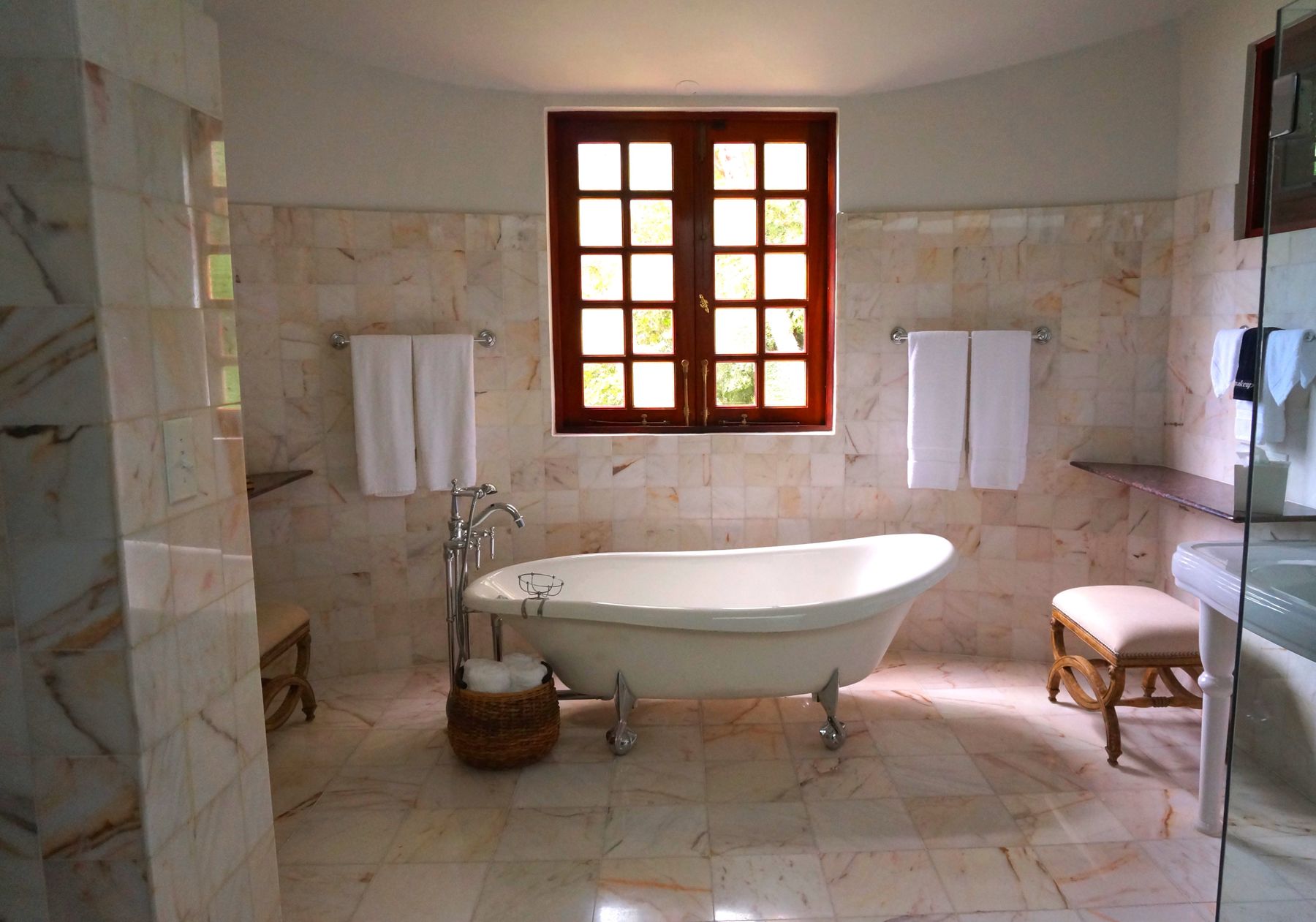 White tiled bathroom with freestanding bathtub and a warm brown-framed window