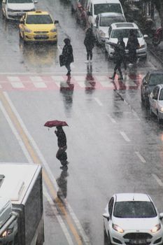People crossing a busy street in the rain, holding umbrellas and walking amidst traffic.