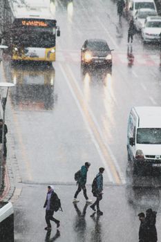 Urban street scene with pedestrians and vehicles during rainfall, highlighting city life in wet weather.