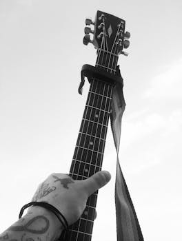 Black-and-white photo of a hand holding an acoustic guitar neck against the sky.