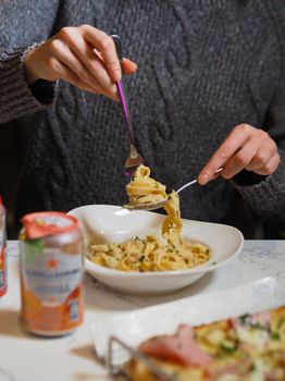 A person enjoying a creamy pasta dish indoors, focusing on the fork and bowl.