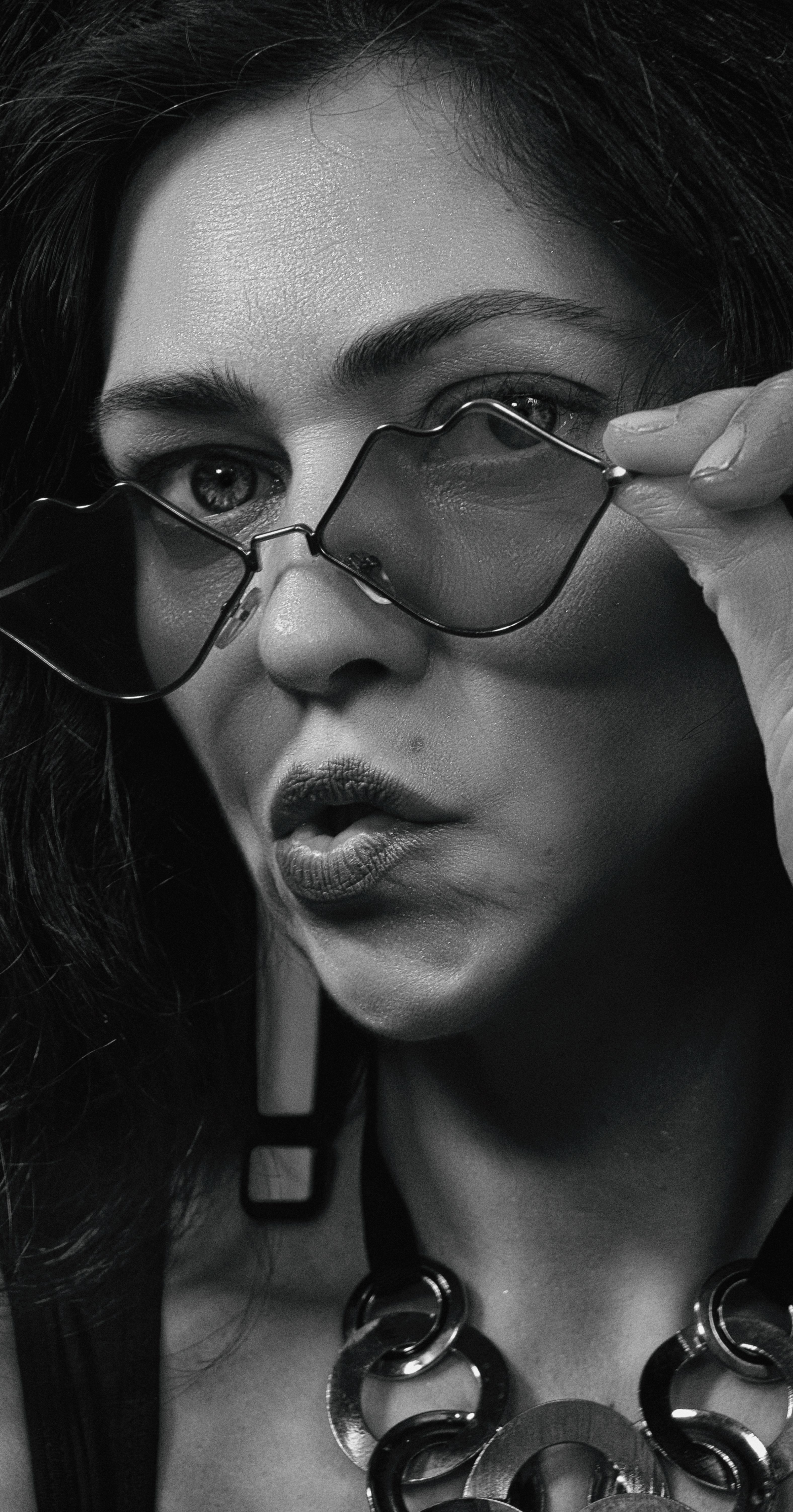 Artistic black and white portrait of a woman adjusting sunglasses with a pout.