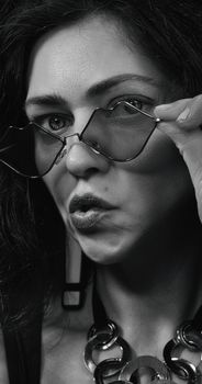 Artistic black and white portrait of a woman adjusting sunglasses with a pout.