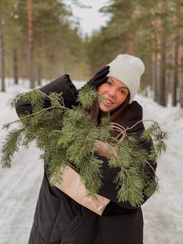 Young woman in winter attire holding pine branches outdoors in a snowy forest.