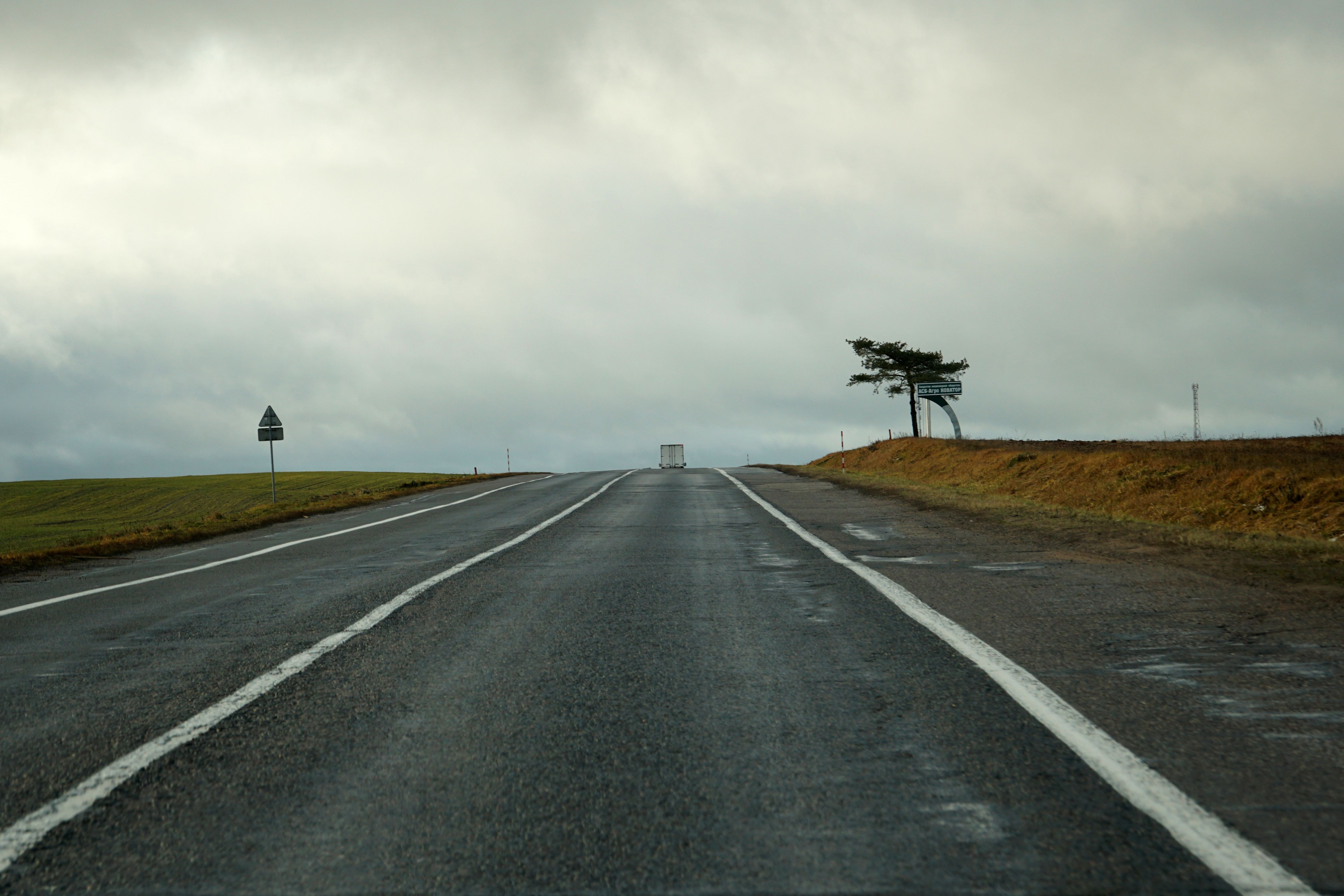 An empty road stretches into the distance under a cloudy sky with a single truck visible on the horizon.