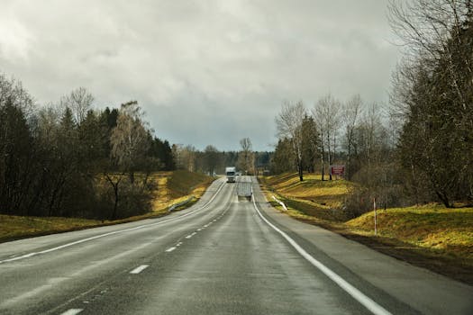 A straight highway with trucks amidst overcast skies and surrounding fields.
