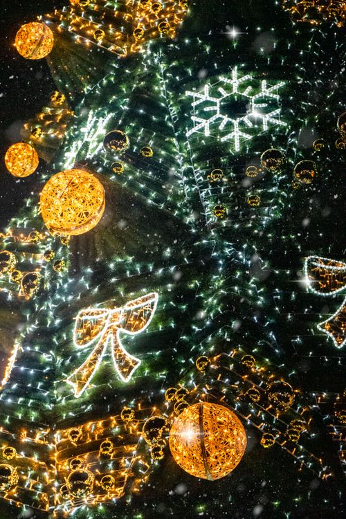 Free Festive Christmas tree decorated with lights and ornaments in a snowy night scene. Stock Photo