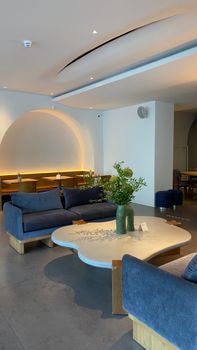 A cozy modern interior featuring blue armchairs, wooden tables, and decorative plants in a brightly lit room.