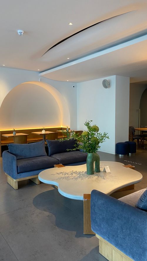 Free A cozy modern interior featuring blue armchairs, wooden tables, and decorative plants in a brightly lit room. Stock Photo