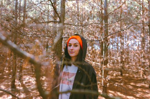 Free A woman in a forest wearing an orange beanie amid leafless trees in autumn. Stock Photo