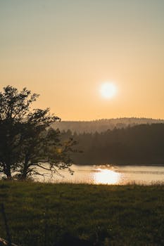 A peaceful sunrise over a quiet lake with distant hills and lush greenery, perfect for nature lovers.