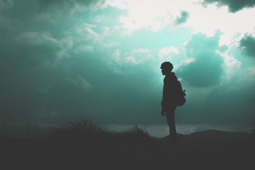 A lone hiker stands silhouetted against a dramatic cloudy sky, creating an atmospheric scene.
