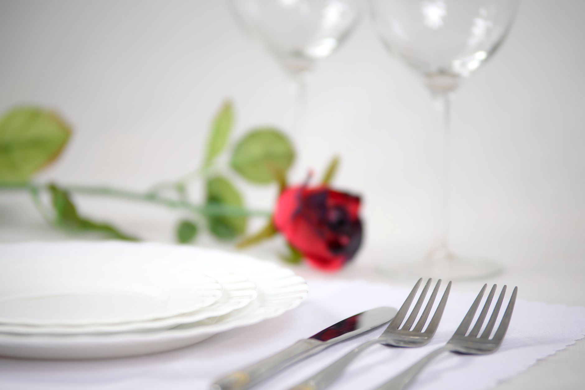 An elegant table setup featuring a red rose, cutlery, and wine glasses for a romantic dinner.