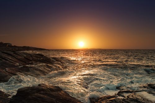 Free Capture of a breathtaking sunset over rocky coastline with waves crashing and a warm glow. Stock Photo