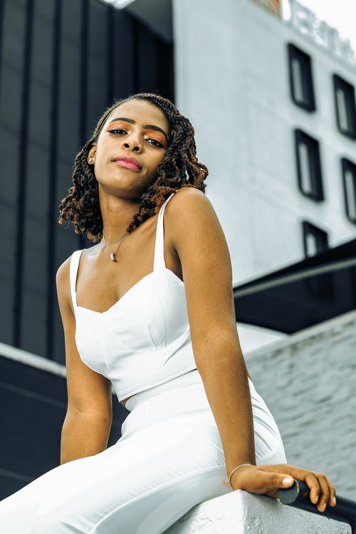 Free A confident woman in a stylish white outfit sits outdoors in an urban setting, exuding elegance. Stock Photo