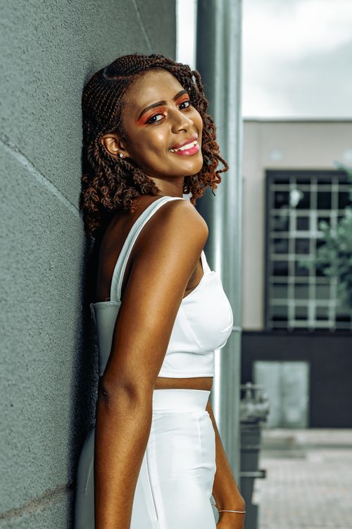Free Portrait of a smiling young woman leaning against a wall in a modern setting. Stock Photo