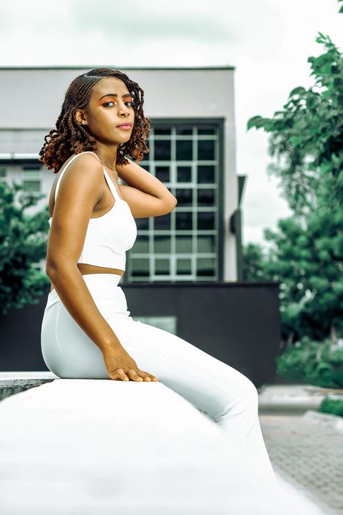 Free Chic woman in white attire poses confidently outdoors against a contemporary architectural backdrop. Stock Photo