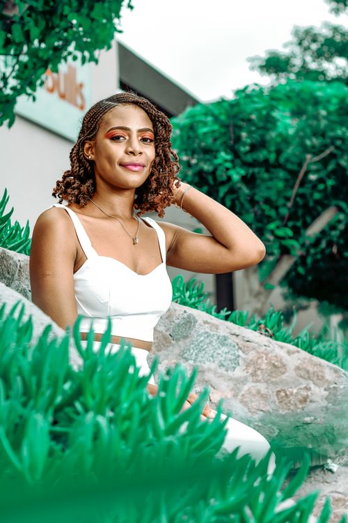 Free A beautiful woman in a white outfit sits outdoors surrounded by greenery, radiating confidence and elegance. Stock Photo