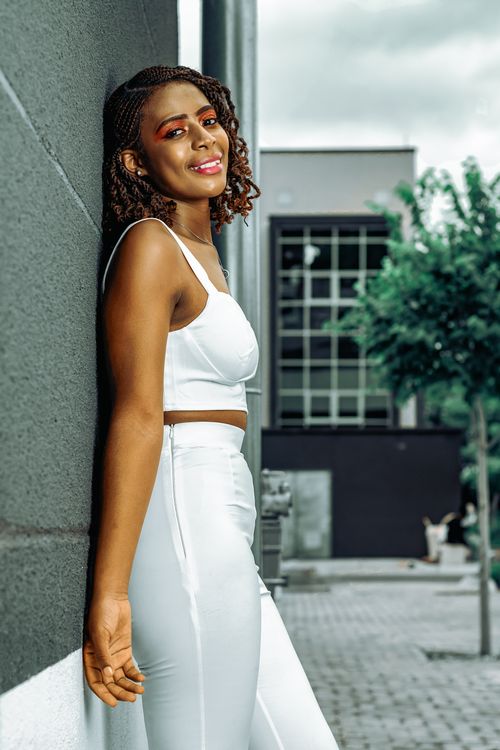Free Portrait of a beautiful African American woman in white clothing leaning against a wall outdoors. Stock Photo