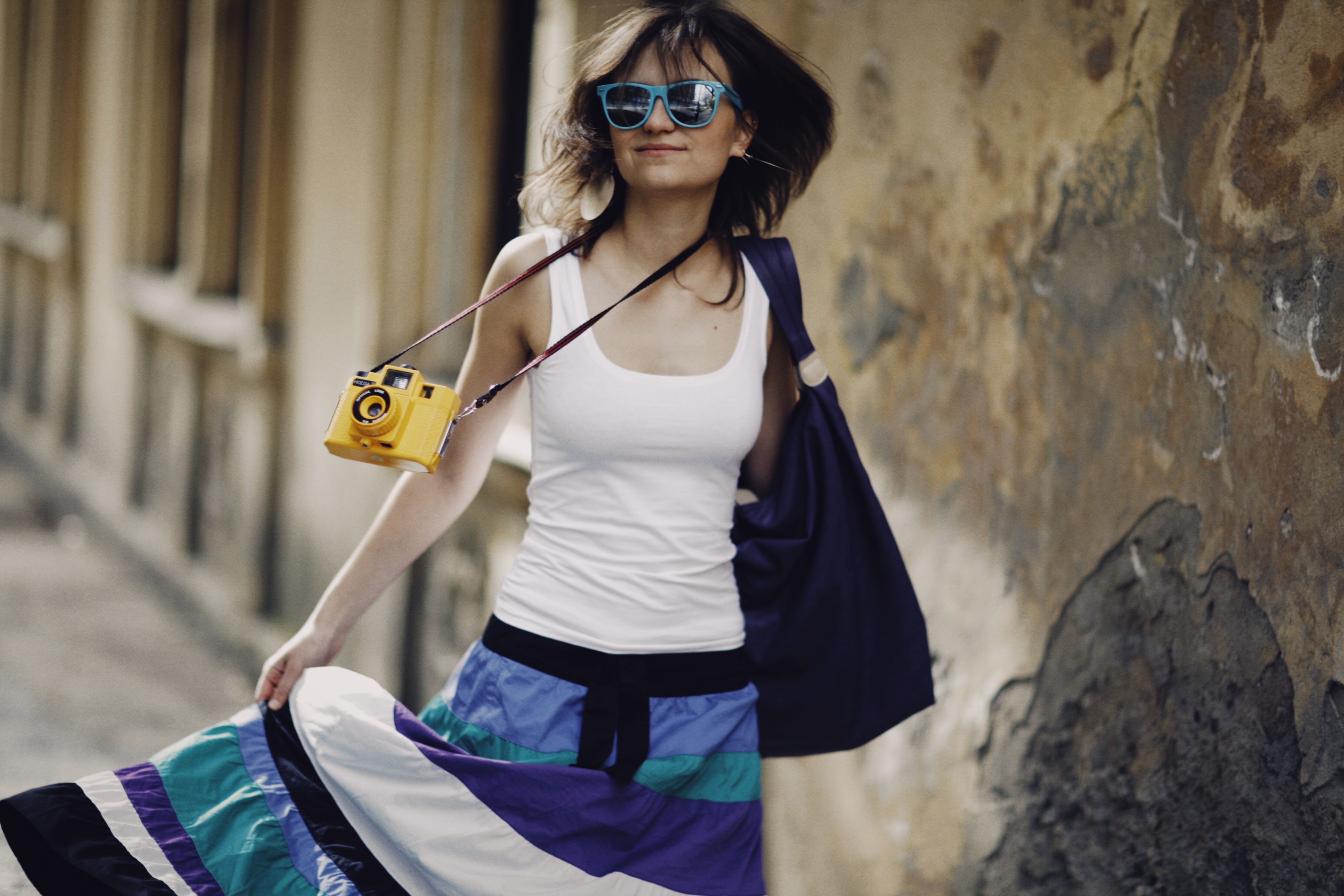 Carefree young woman in a white tank top and colorful skirt, strolling outdoors with a vintage camera.
