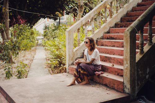 Free Woman with tattoos sitting barefoot on stairs surrounded by lush greenery. Stock Photo