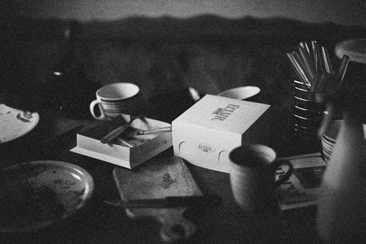 Monochrome still life featuring kitchenware and a box on a cluttered tabletop.