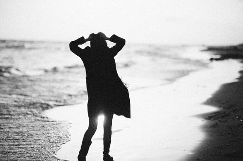 Free Black and white silhouette of a woman standing by the ocean shoreline at dusk, capturing a moment of solitude. Stock Photo