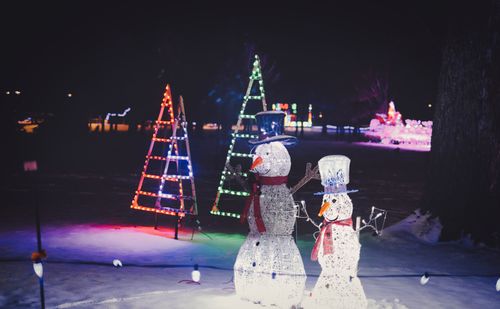 Free Illuminated snowman and holiday lights in a winter night setting, creating a festive atmosphere. Stock Photo