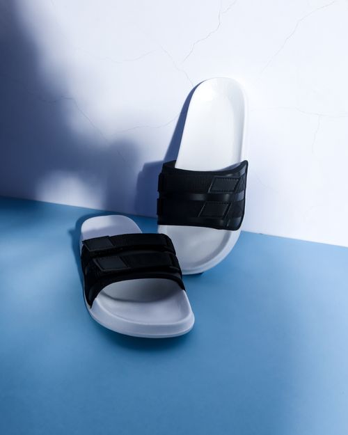 Free Modern black and white slip-on sandals displayed on a blue background with dramatic shadows. Stock Photo
