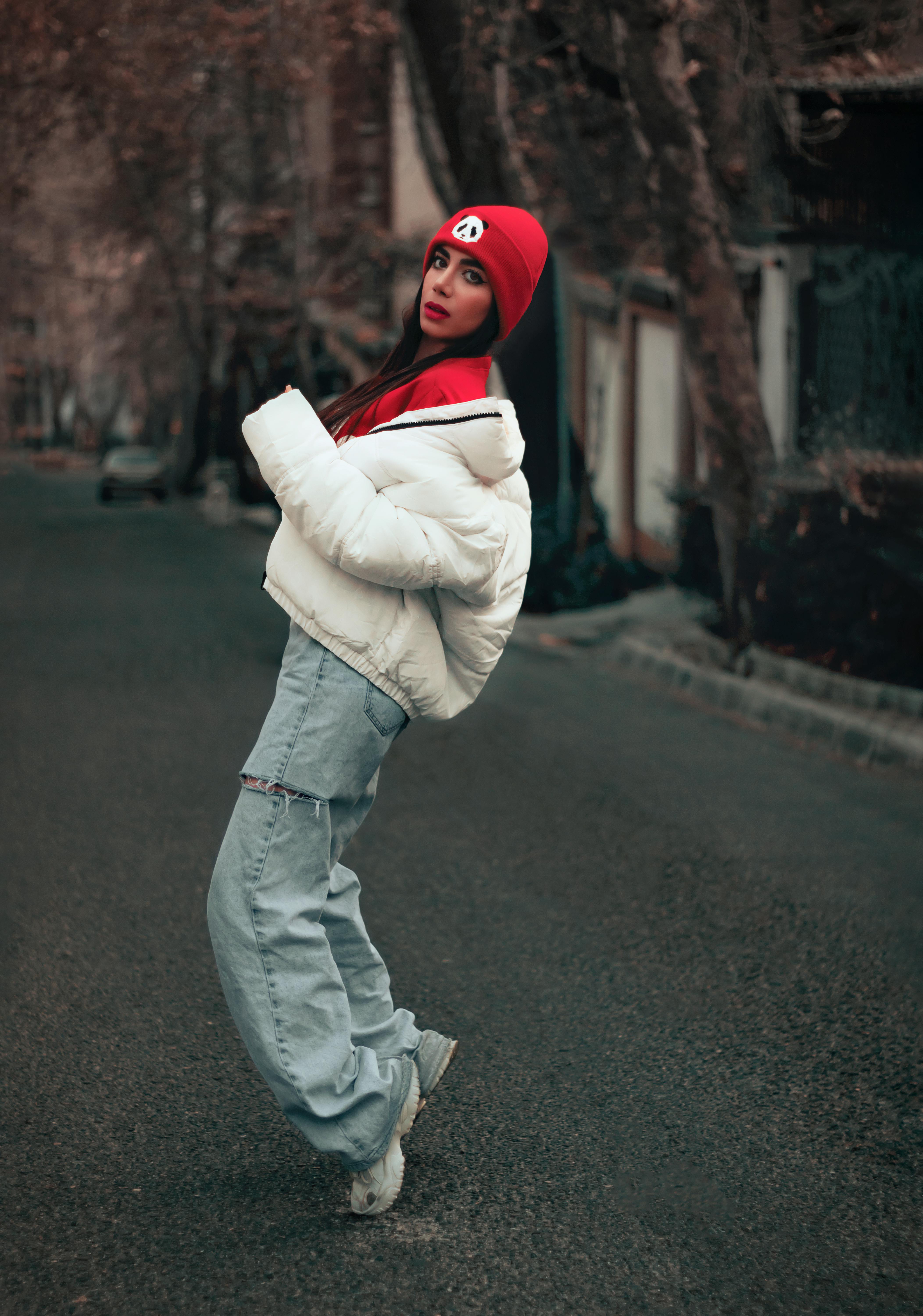 Free Fashionable woman posing in street with white jacket and red beanie, urban style. Stock Photo