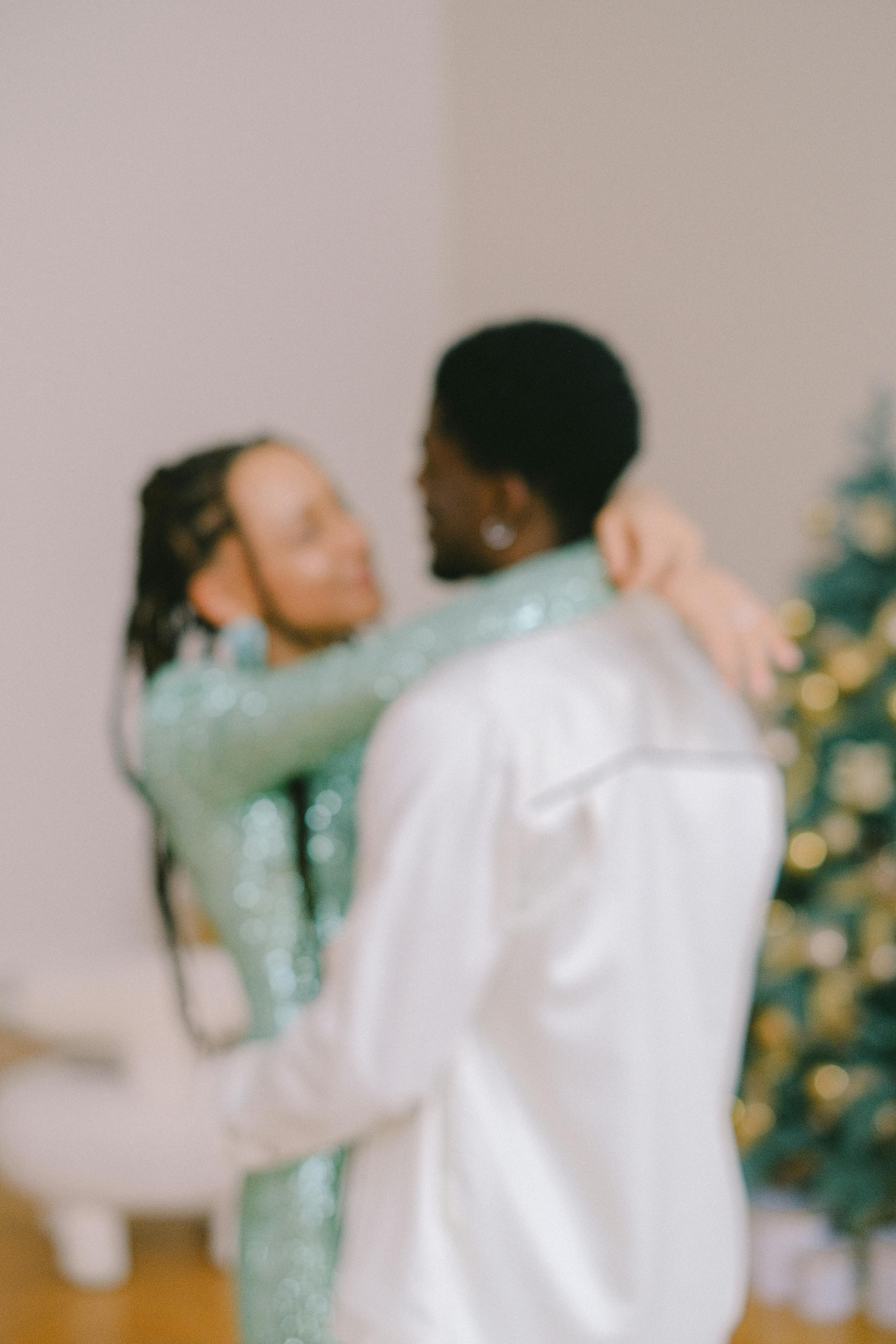 Happy interracial couple embracing near a decorated tree, celebrating love.