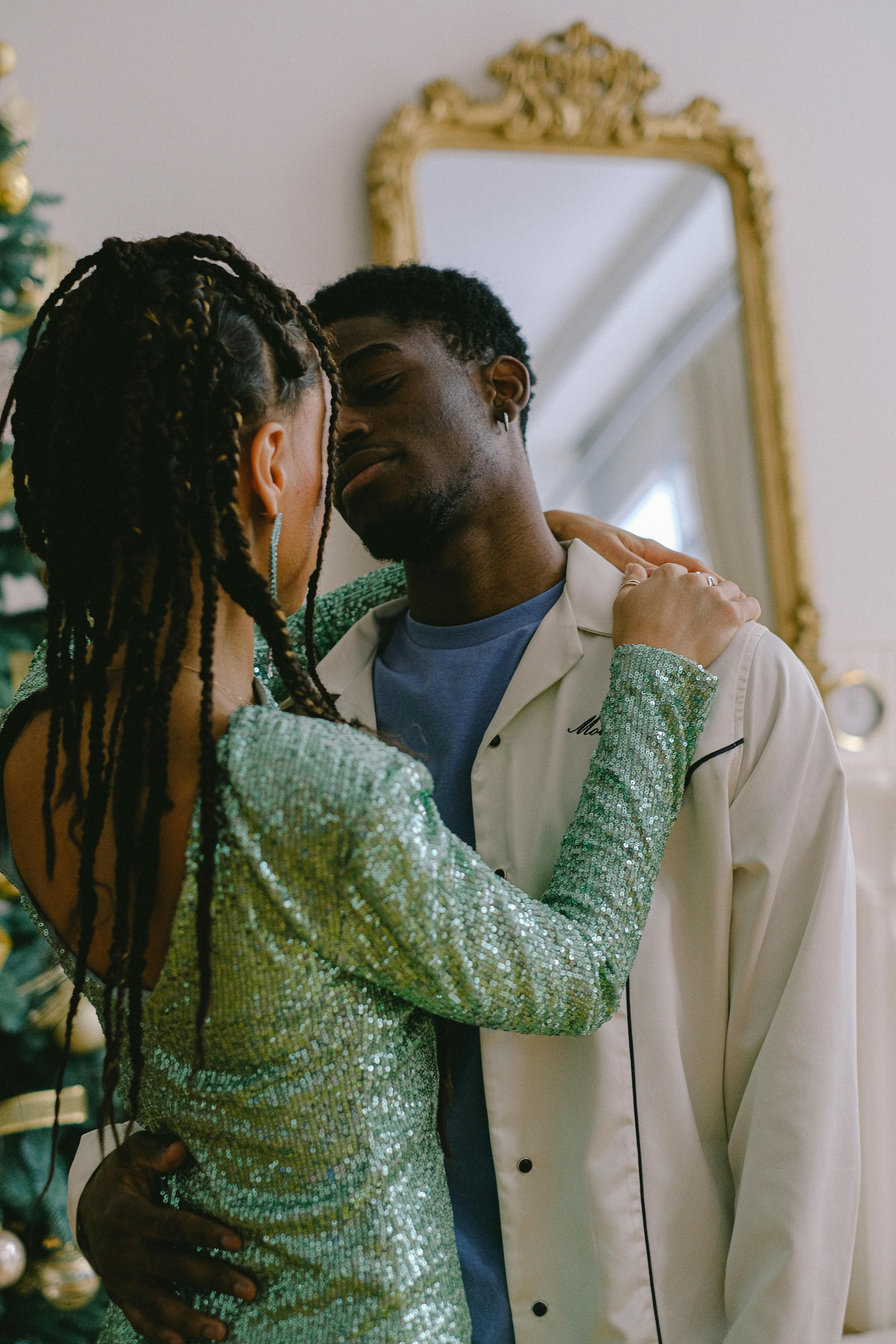 A couple sharing a tender embrace in a festive indoor setting with Christmas decor.