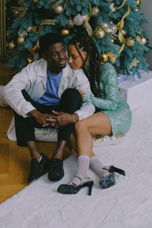 Free A couple sitting closely together by a Christmas tree, creating a warm festive atmosphere. Stock Photo