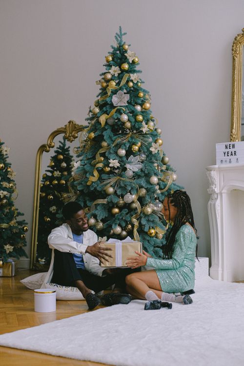 Free A joyful couple exchanging gifts beside a beautifully decorated Christmas tree indoors. Stock Photo