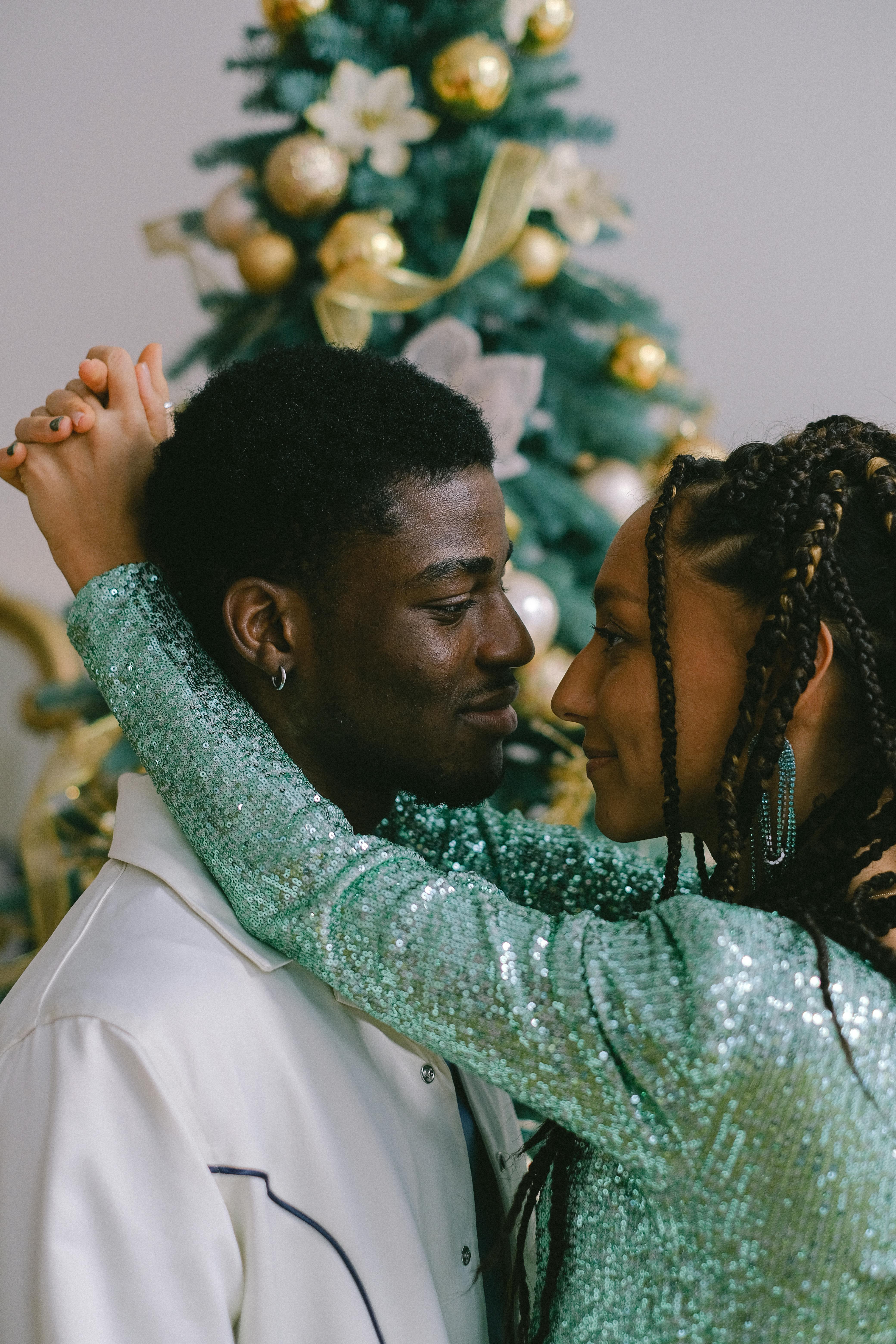 A tender moment shared by a loving couple standing in front of a festive Christmas tree.