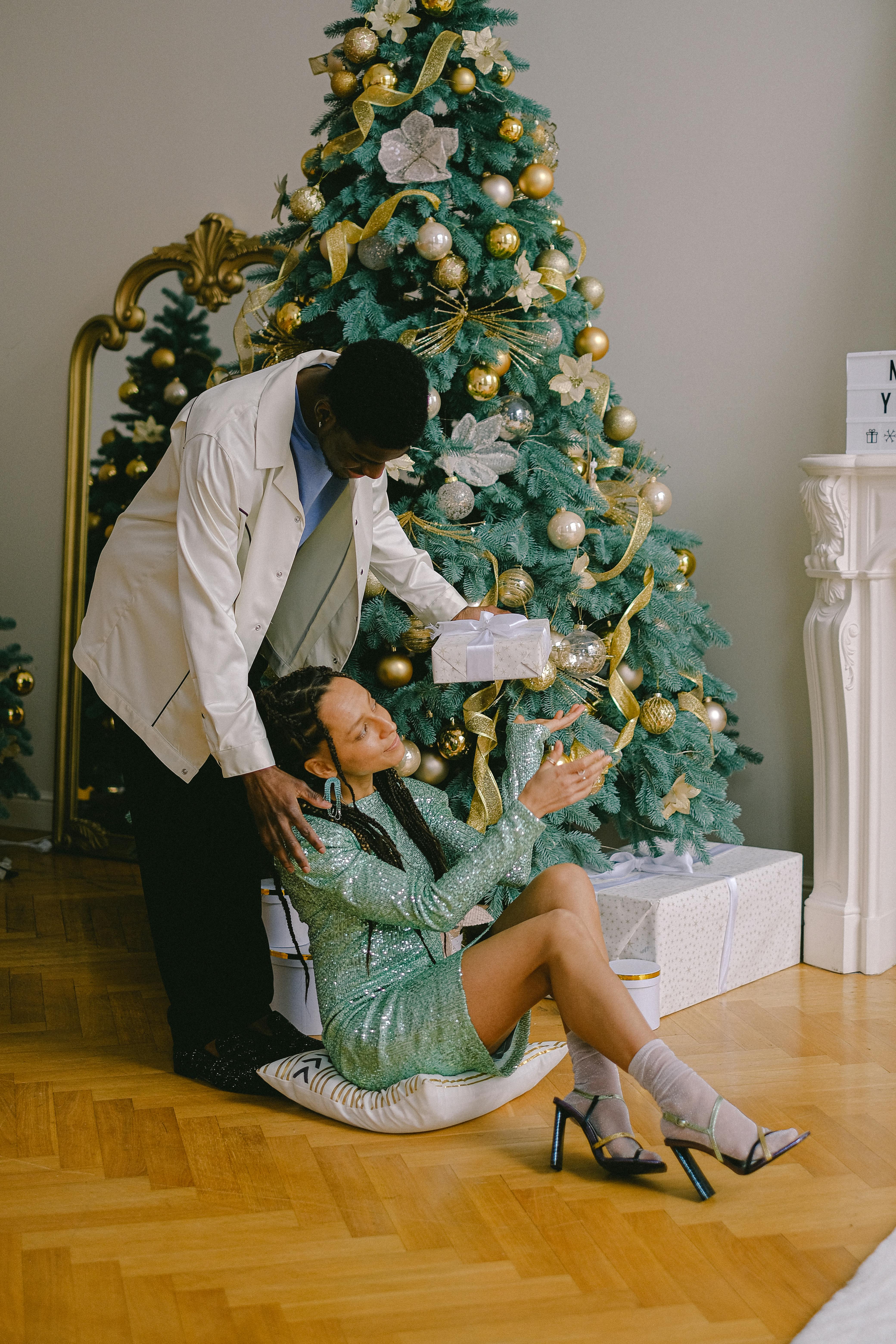 Festive scene of a joyful couple exchanging gifts by the Christmas tree indoors.