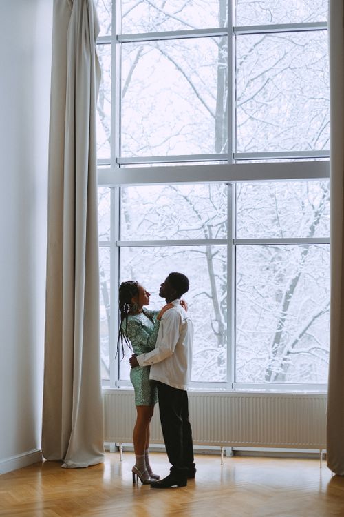 Free A couple stands in an elegant room with a snowy backdrop, capturing a romantic moment. Stock Photo