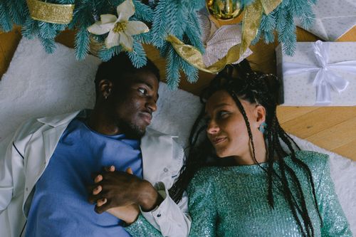 Free Couple lying under decorated Christmas tree, sharing a tender moment of love and connection. Stock Photo