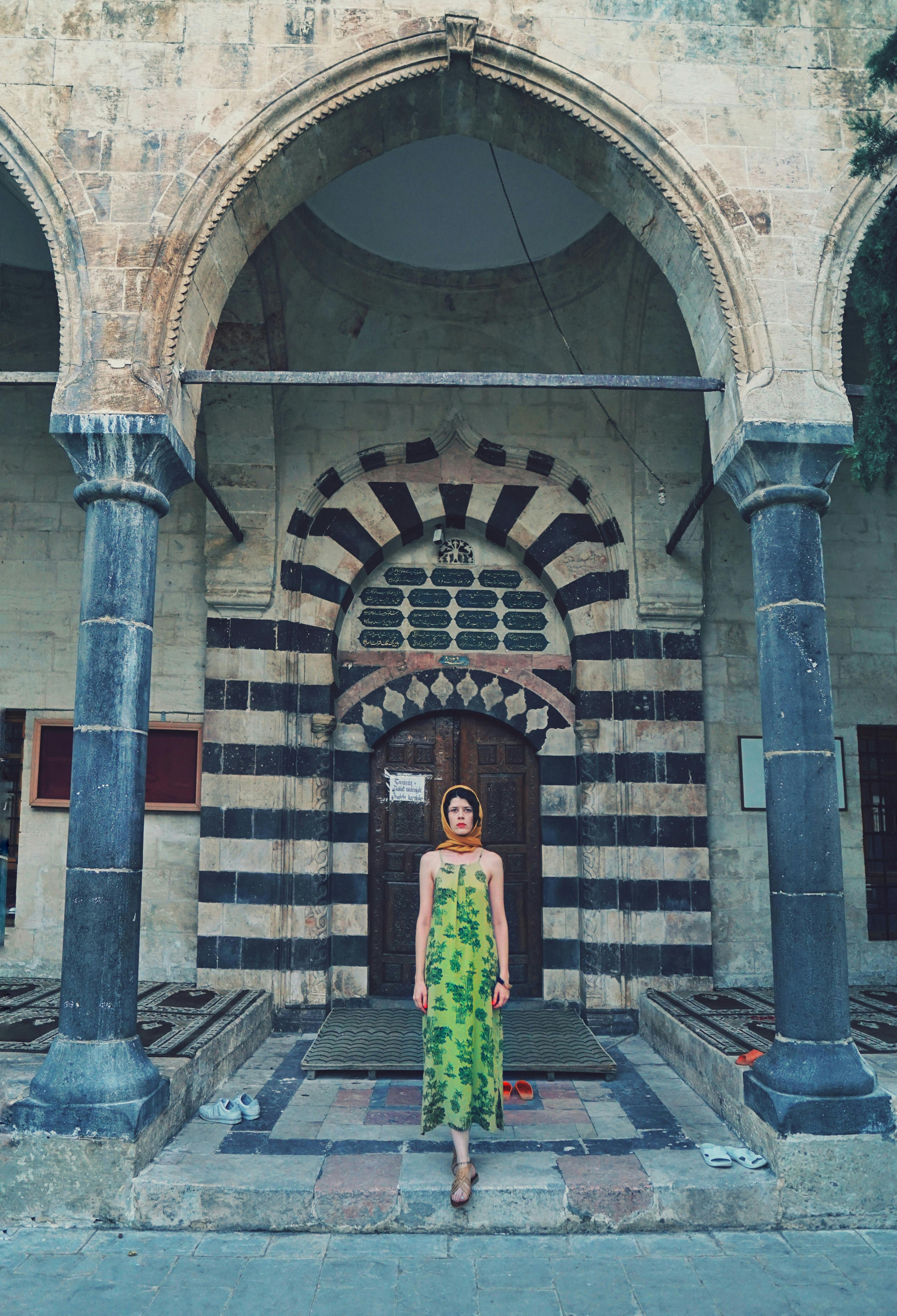 A woman in a green dress stands at a historic architectural entrance with arches and a patterned facade.