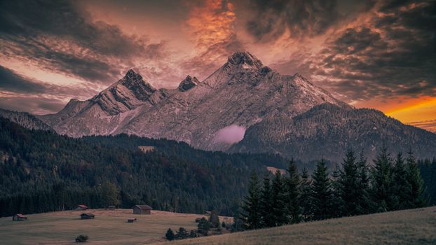 Stunning view of a mountain range with dramatic sunset colors over a serene forest landscape.