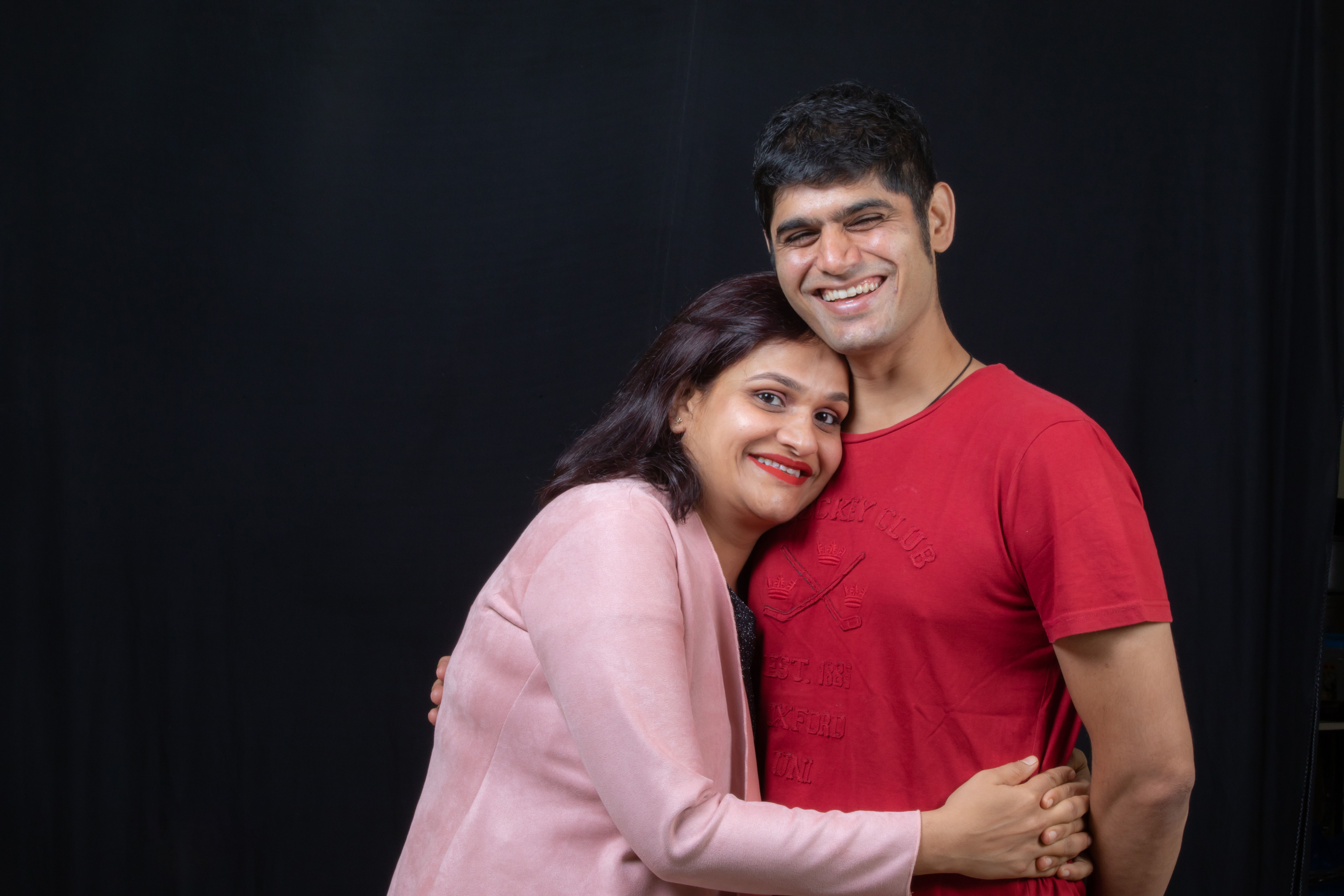 Joyful couple sharing a warm embrace and smiles against a dark background.