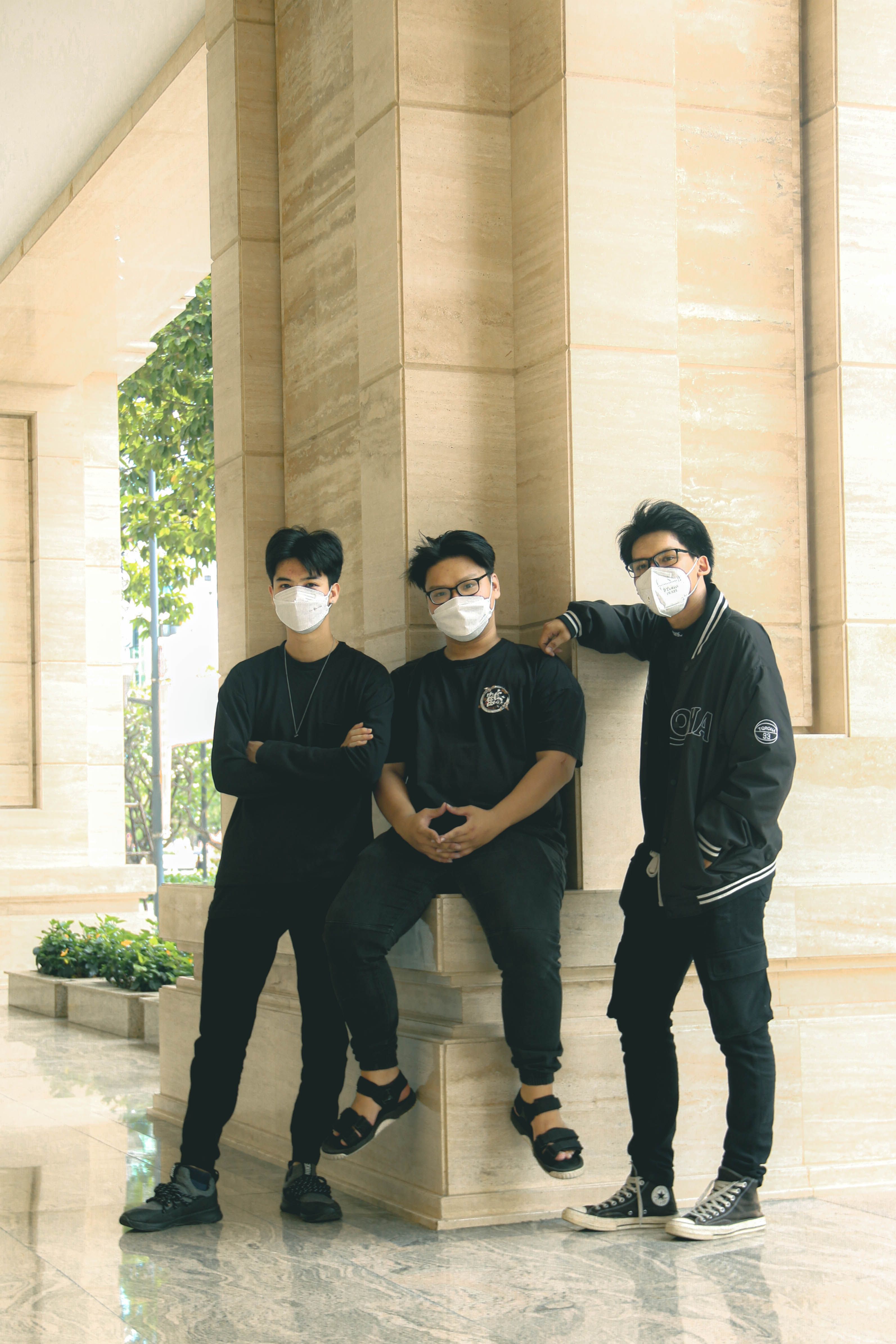 Group of three friends in face masks posing indoors with a marble background.