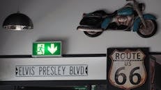 室内装饰风格复古，设有猫王大道标志、66号公路标志，墙上还挂着一辆老式摩托车