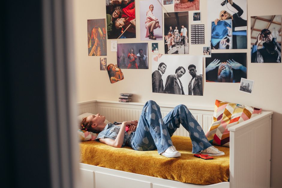 A young woman lies on her bed in a stylish room with creative wall art and cozy decor.