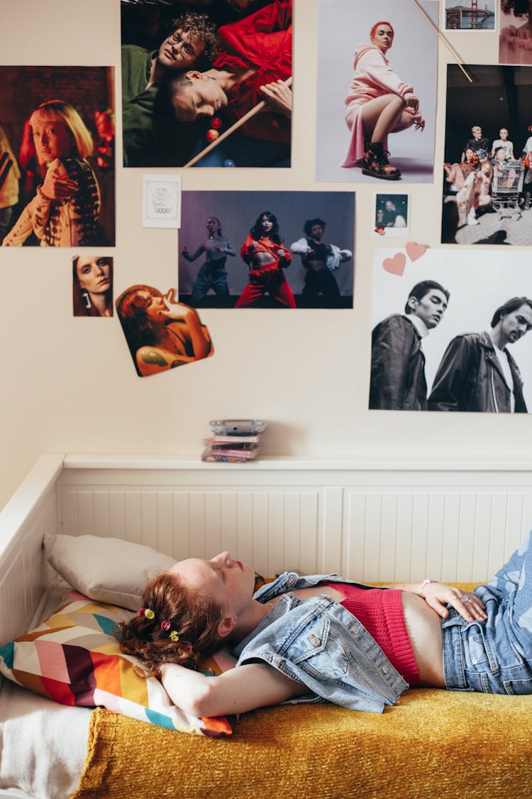 A Woman Wearing Denim Jacket Lying On Bed Near White Wall With Pictures