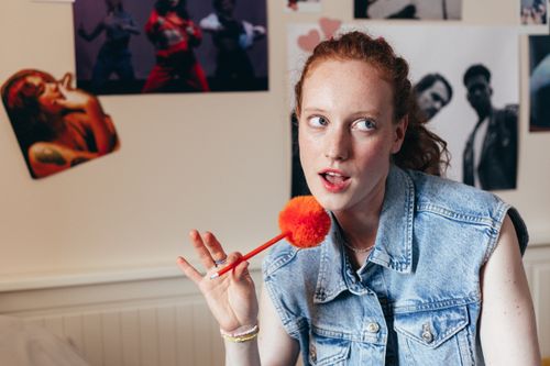 Free Redheaded woman in denim vest holds colorful pen, expressing creativity. Stock Photo