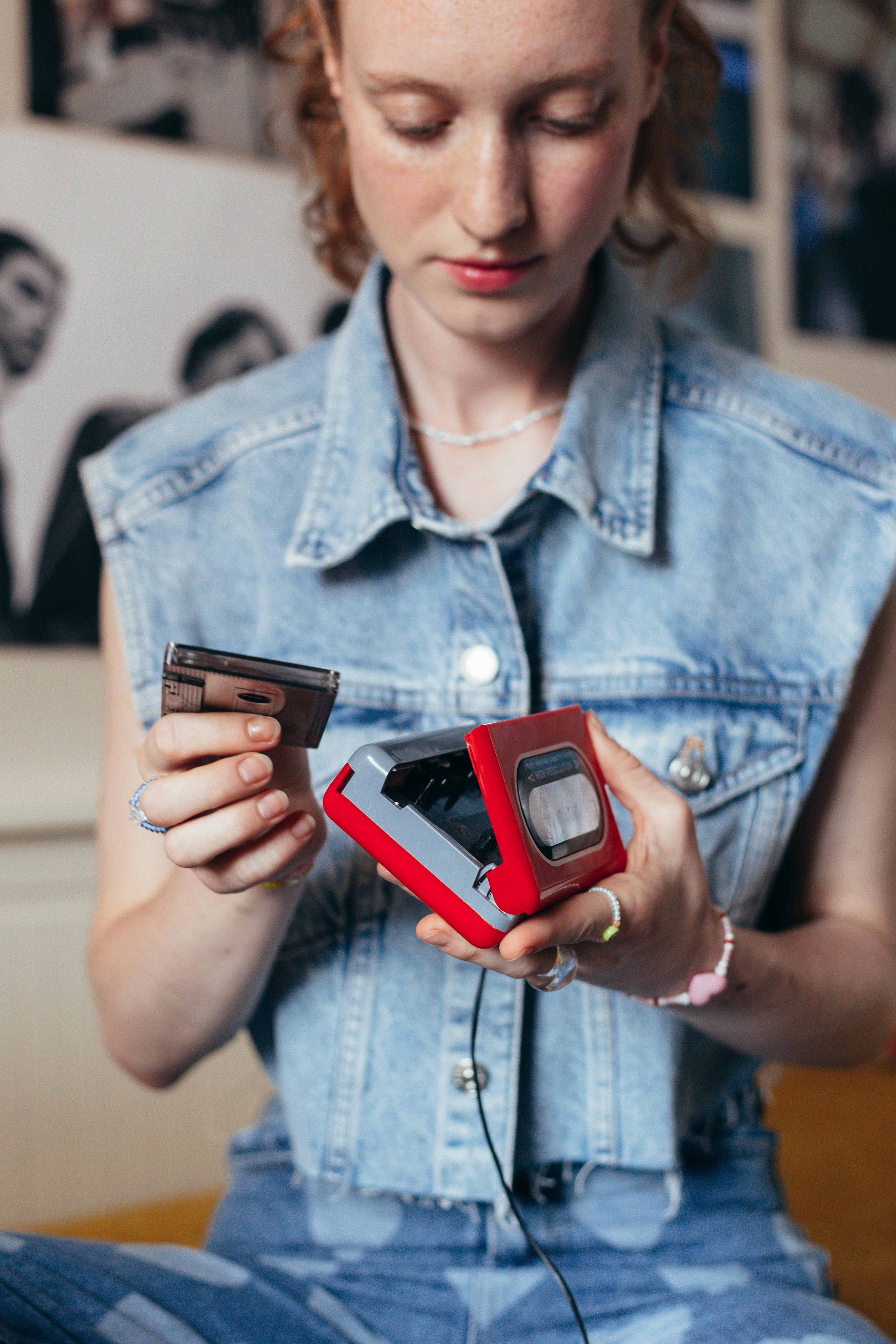 woman in blue denim button up jacket holding a cassette player and tape