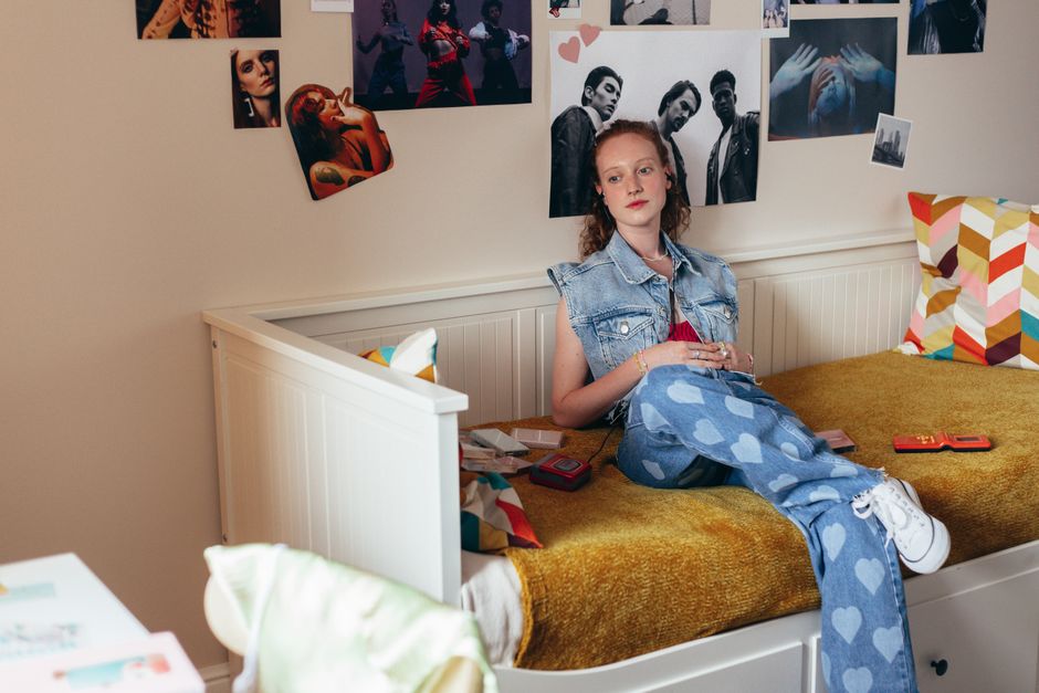 Teen girl in a stylish bedroom wearing denim outfit surrounded by posters.