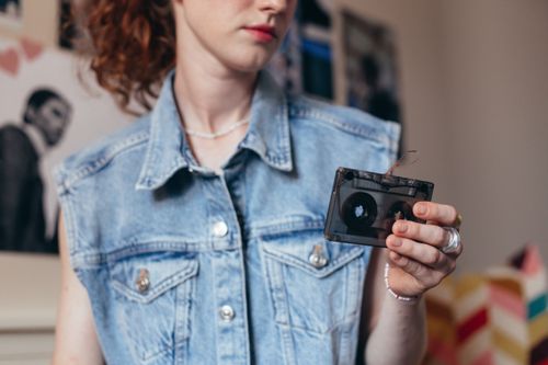 Free Young woman holding a cassette tape, wearing a vintage denim vest, evoking retro vibes. Stock Photo